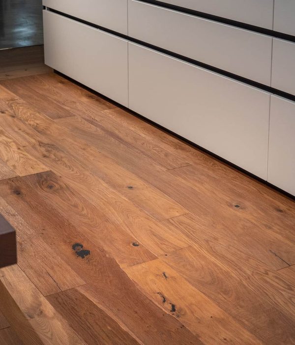 Pavimento in legno naturale per interni con venature visibili, posato in una cucina moderna dai mobili bianchi.